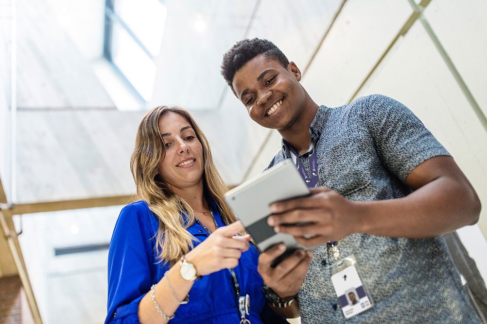 Two colleagues smiling while reviewing information on a tablet in a bright office.