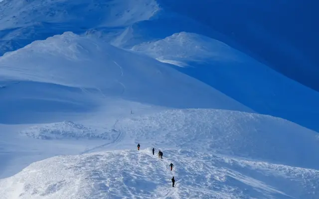 Group of explorers hiking along the summit of a frozen mountain.