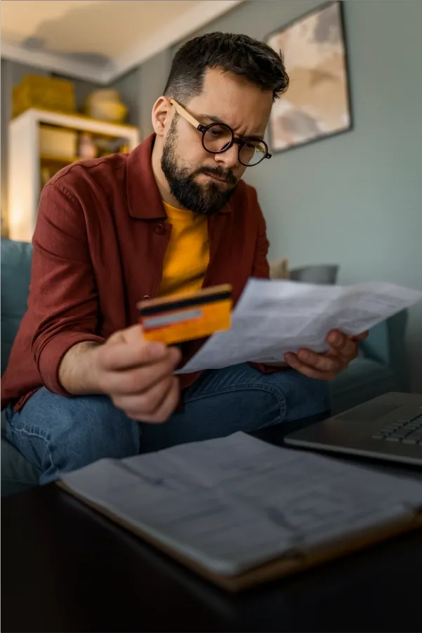 Man reviewing a bill while holding a credit card at home.