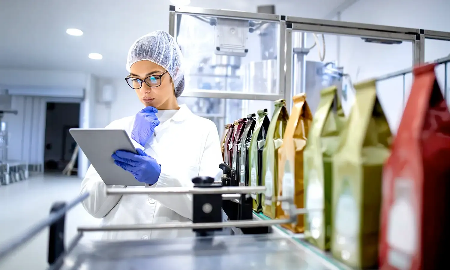 Quality technician inspecting packaged products on a production line using a tablet.