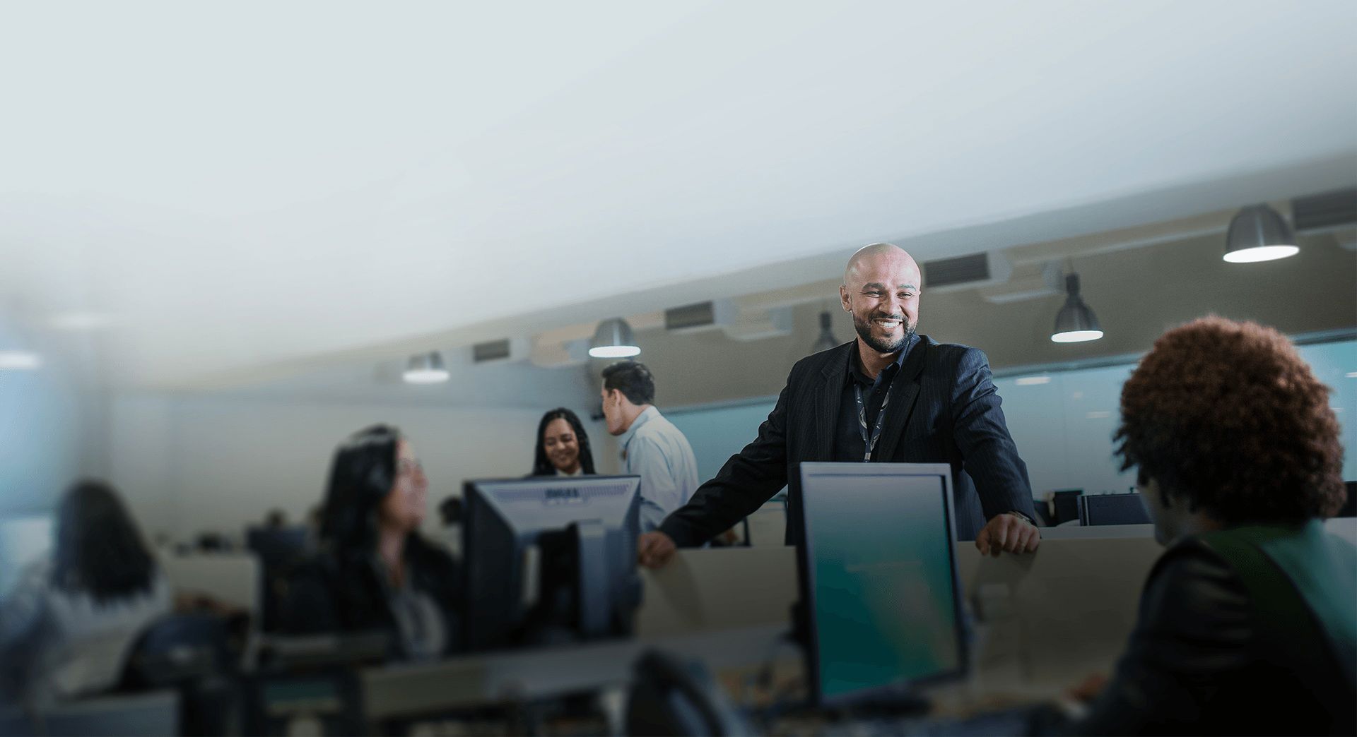 Team leader collaborating with colleagues in a modern office, discussing work at computer stations.