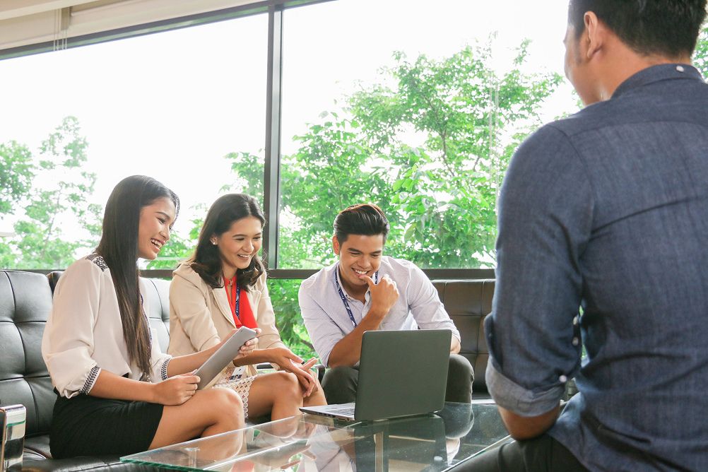 Colleagues reviewing a tablet and laptop during a team meeting in a bright office.