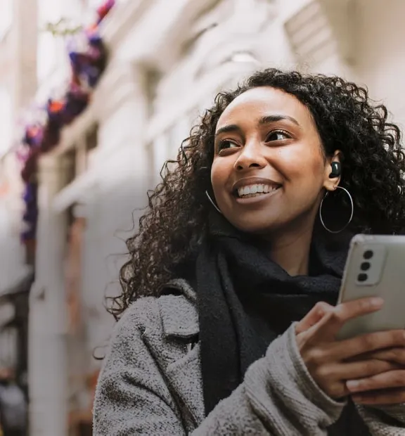 Smiling African young woman walking on the streets while listening to music through her earphones