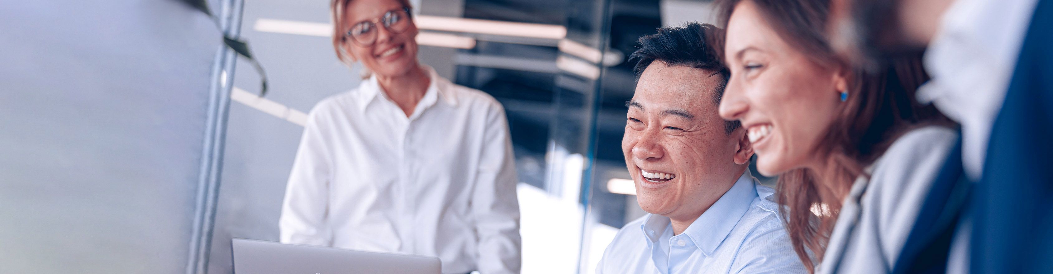 A diverse team of professionals laughs joyfully together in a bright modern office